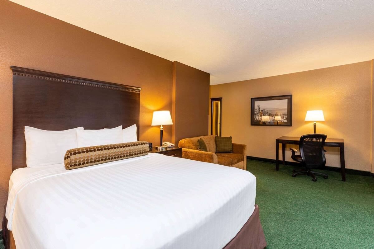 A hotel room with a large bed, two bedside lamps, a chair, a desk, and a framed picture on the wall.