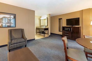 Quarto de hotel com área de refeições, televisão, micro-ondas e banheiro com pia e espelho.