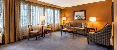 A hotel room with a sofa, armchair, and a small table with chairs.