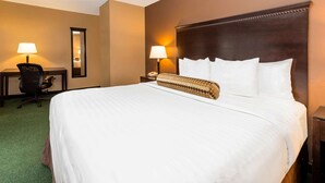 A hotel room with a large bed, two bedside lamps, a desk with a chair, and a mirror on the wall.