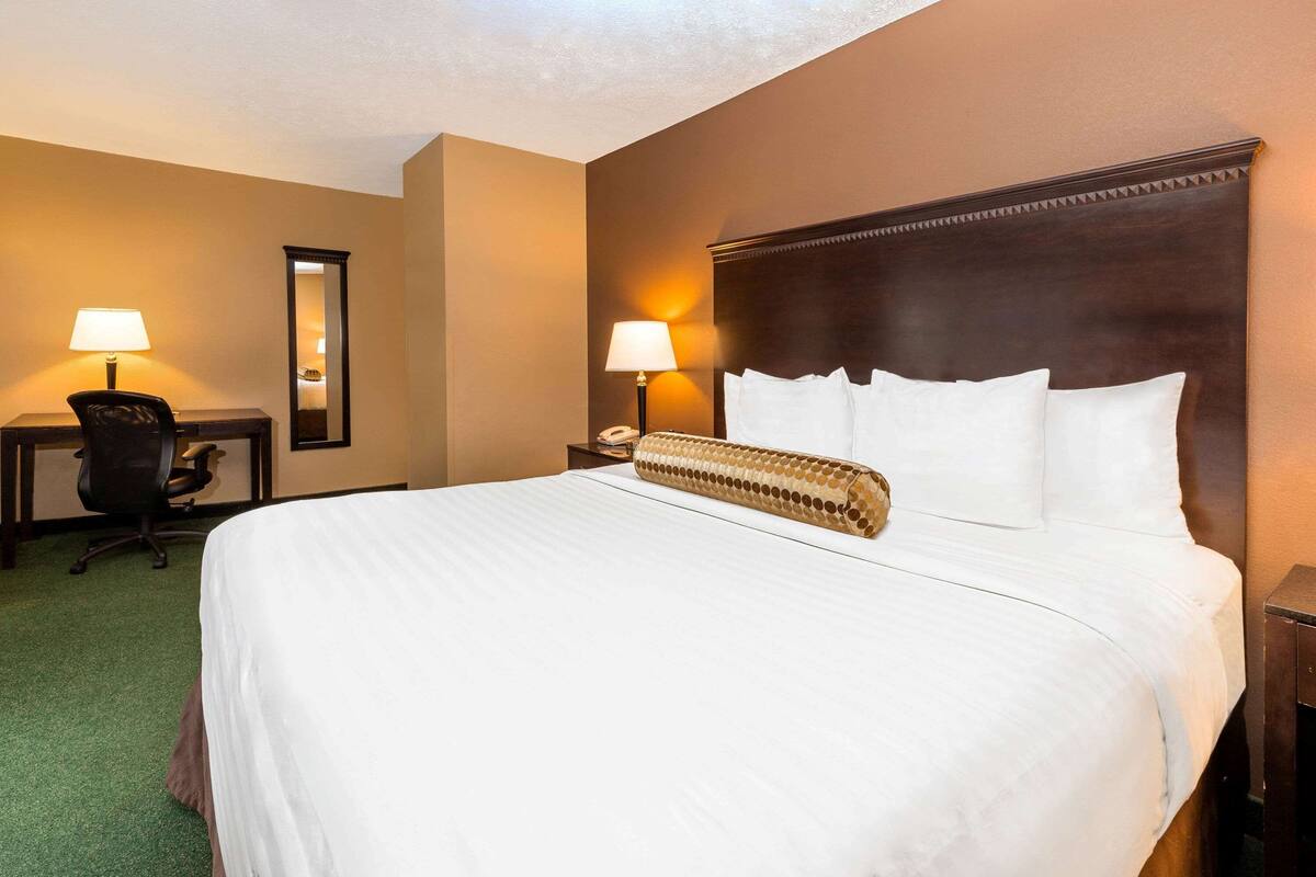 A hotel room with a large bed, two bedside lamps, a desk with a chair, and a mirror on the wall.