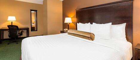 A hotel room with a large bed, two bedside lamps, a desk with a chair, and a mirror on the wall.