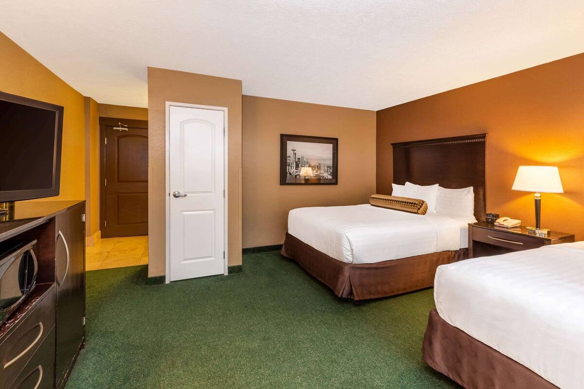 A hotel room with two beds, a television, a desk with a lamp, and a framed picture on the wall.