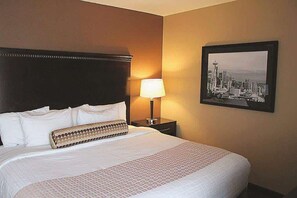Quarto de hotel com uma cama grande, cabeceira, mesa de cabeceira com abajur e uma pintura emoldurada com vista para a cidade.