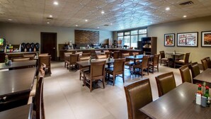 A spacious dining area with multiple tables and chairs, a kitchen in the background, and a ceiling with a unique circular pattern.