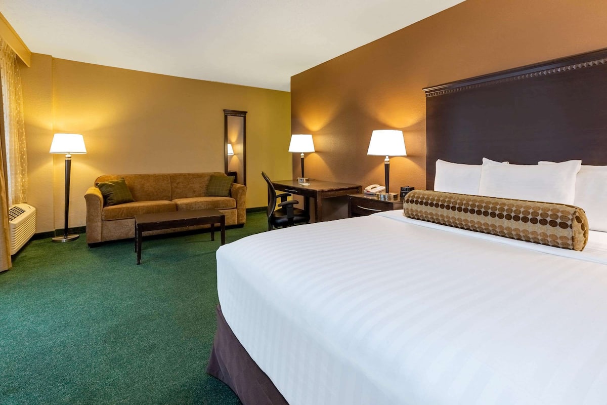 A hotel room with a large bed, a sofa, two lamps, a desk, and a telephone.