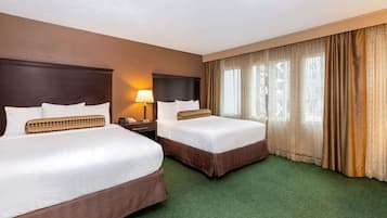 A hotel room with two beds, a nightstand, a lamp, and a window with curtains.