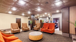 A lobby with a round ottoman, several armchairs, a reception desk, and a clock on the wall.