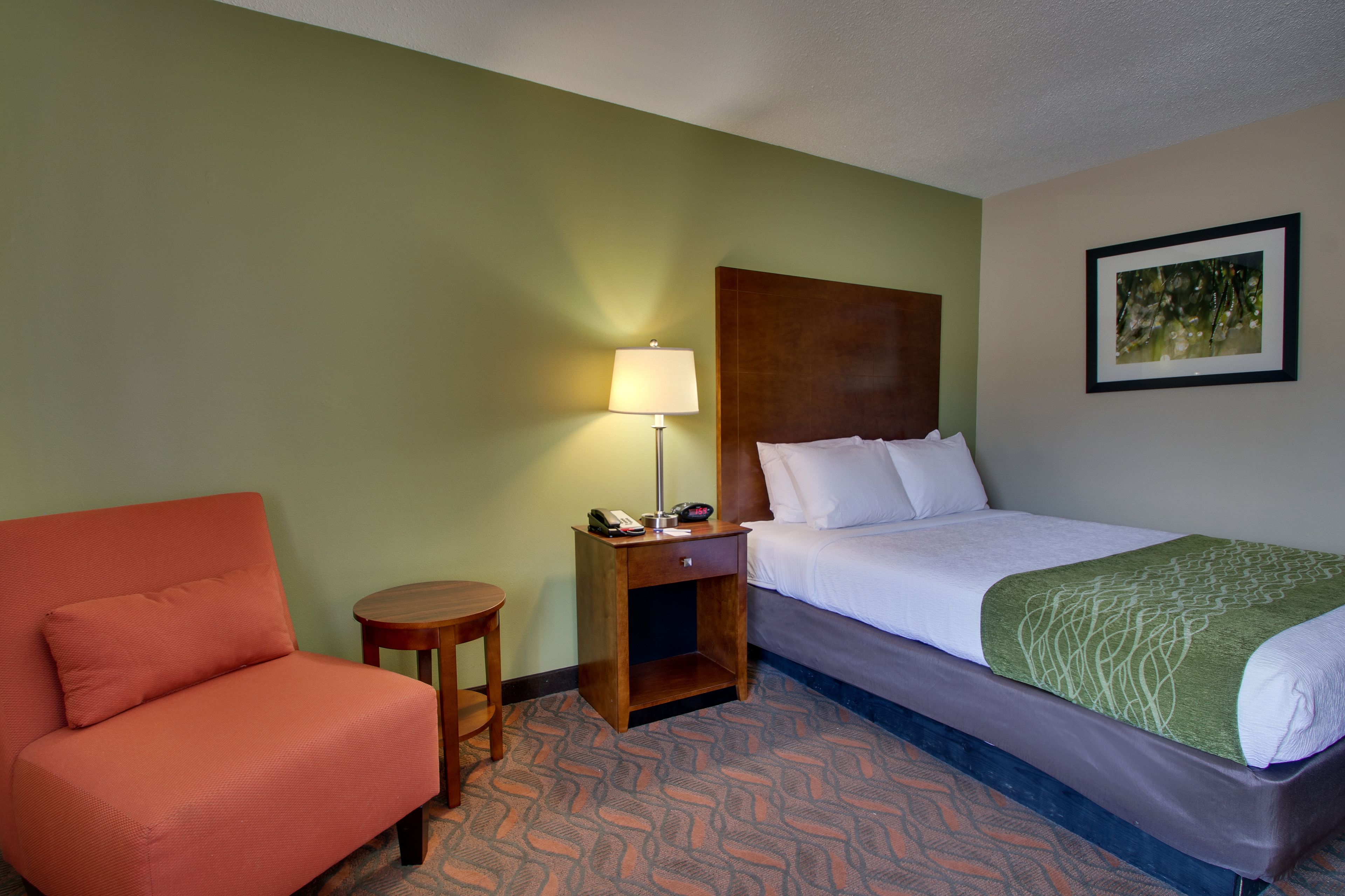 Une chambre d’hôtel avec un lit, une chaise, une table de chevet avec une lampe et un tableau au mur.