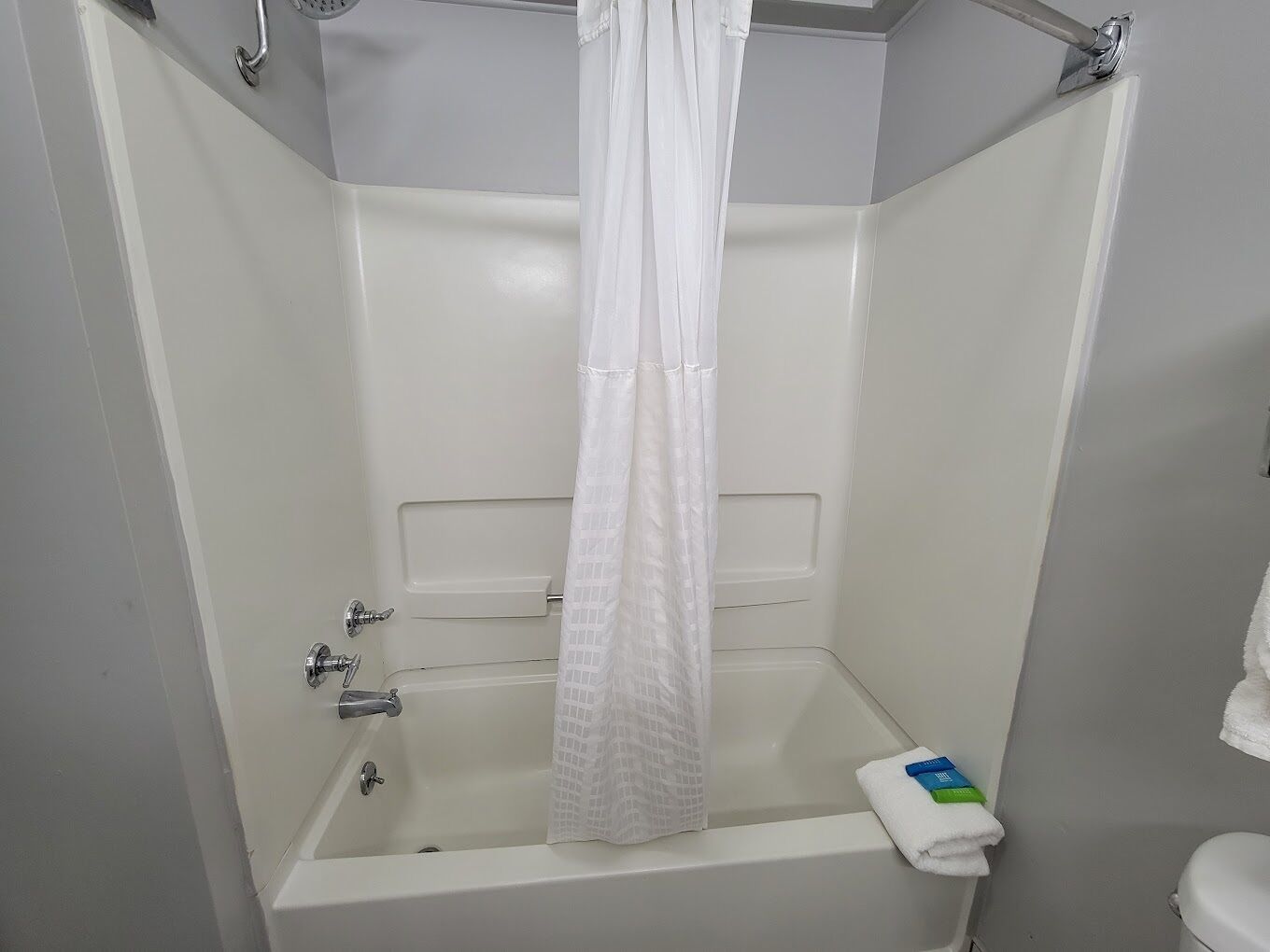 A white bathtub with a shower curtain, a towel, and toiletries.