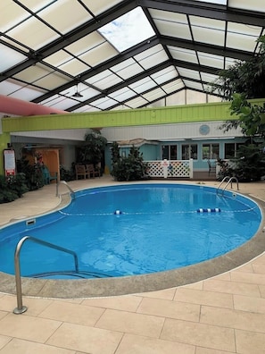 An indoor swimming pool with a glass ceiling, surrounded by a green and white building, and a small seating area with chairs and tables. - Greenfield Inn and Suites Elizabethtown, KY I65 Exit 94 (Elizabethtown)