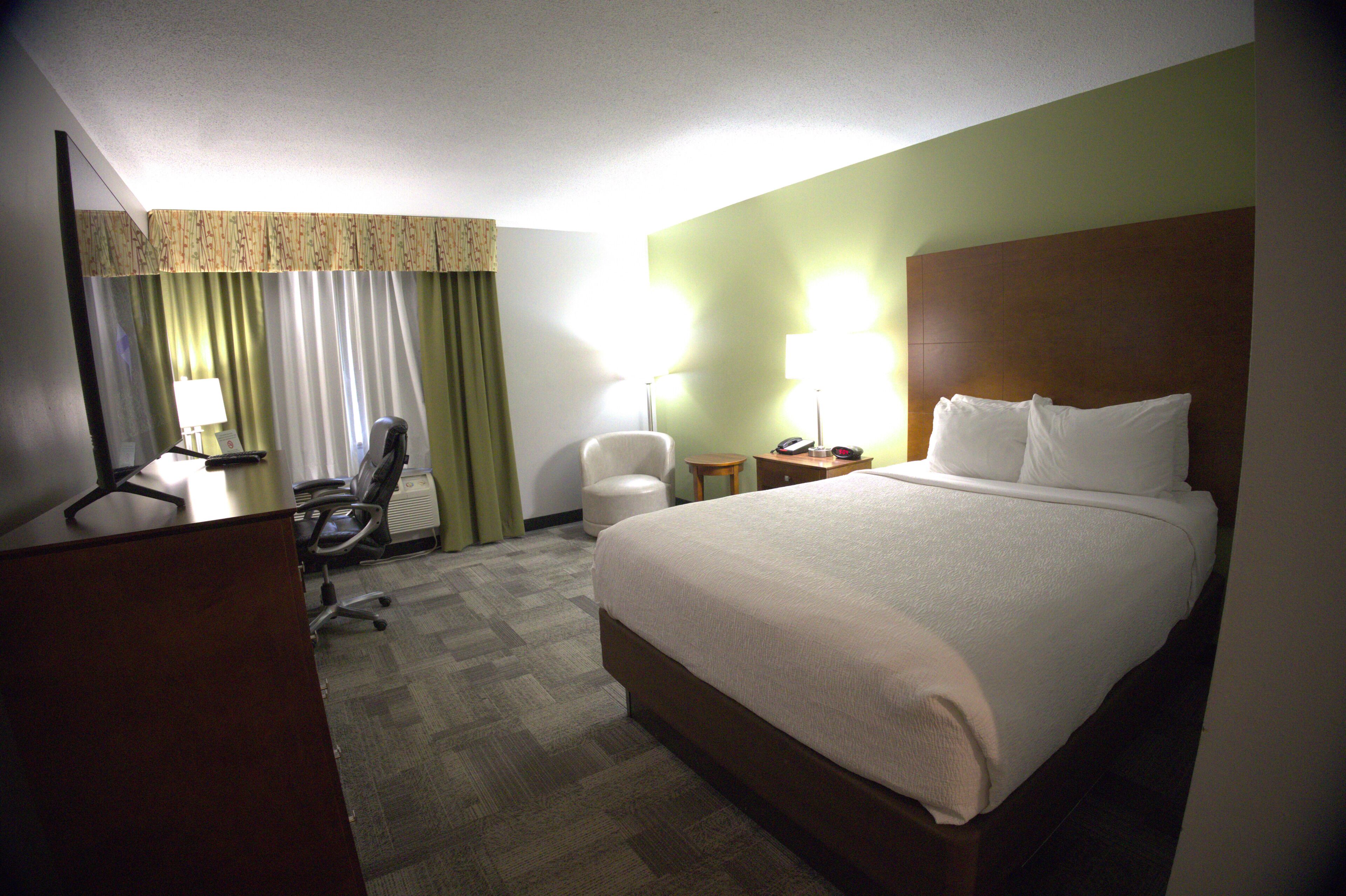 A hotel room with a bed, desk, chair, and lamps.