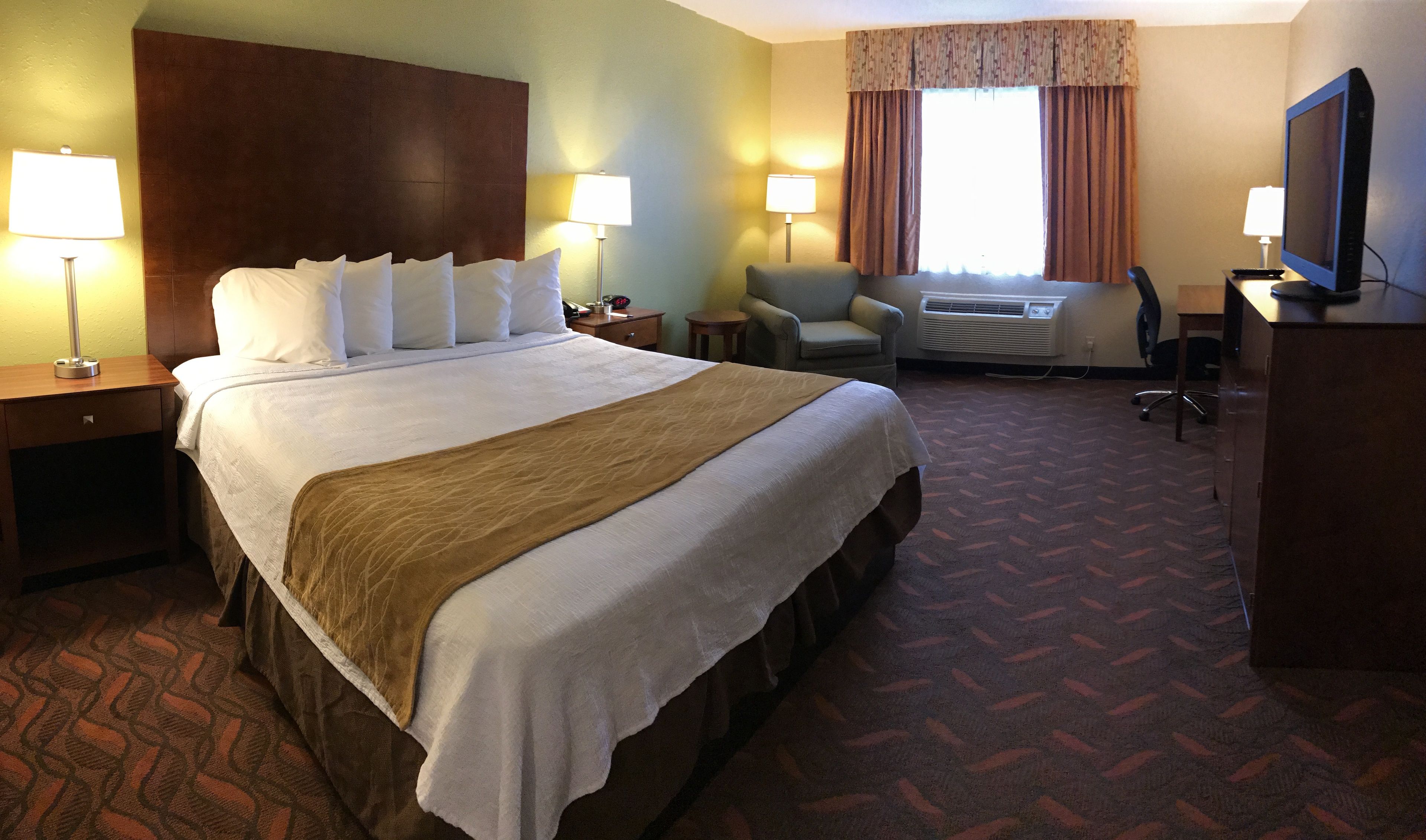 Habitación de hotel con una cama grande, dos mesitas de noche con lámparas, un escritorio con una computadora, un equipo de aire acondicionado y un televisor.