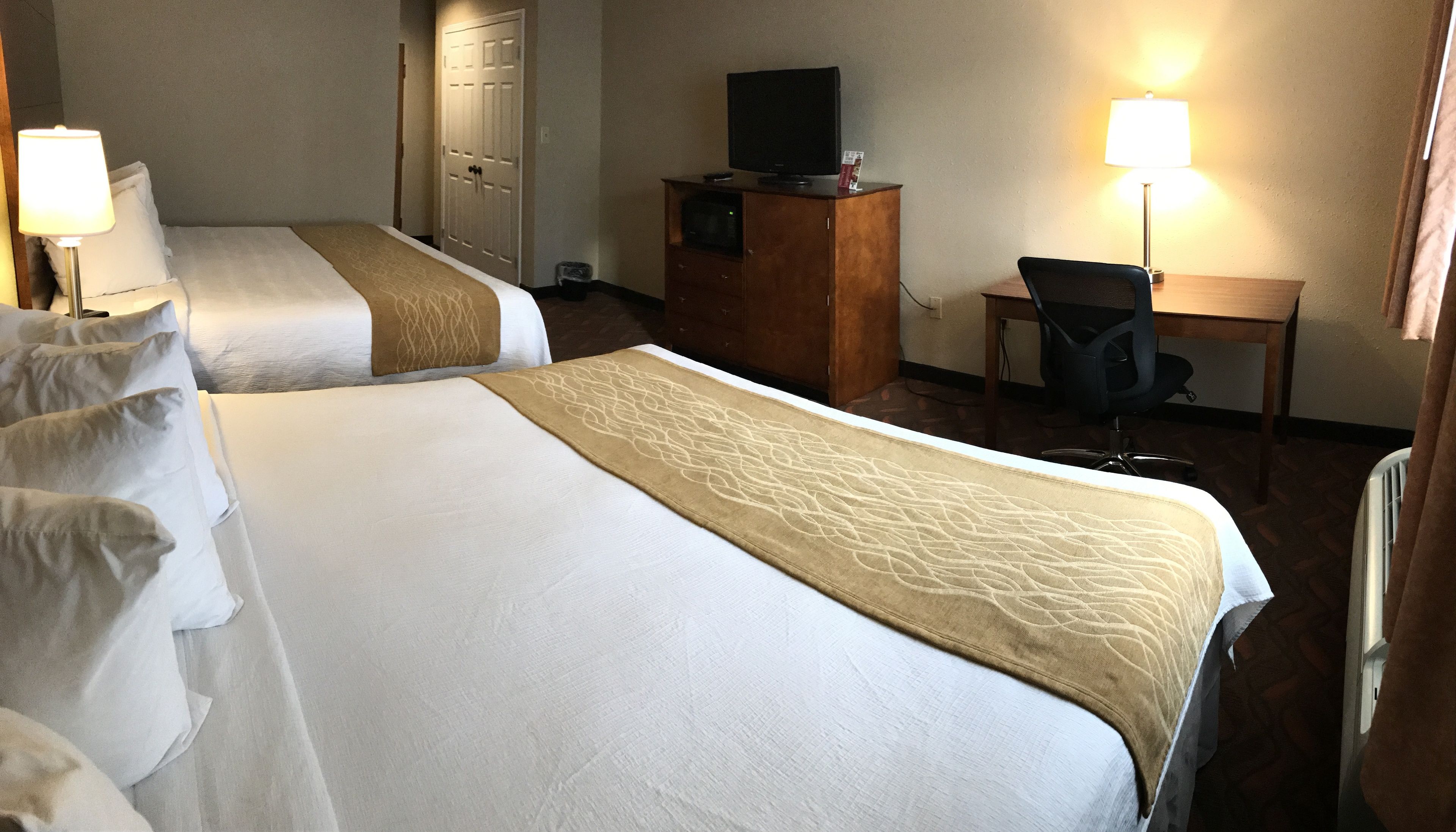 Ein Hotelzimmer mit zwei Betten, einem Schreibtisch, einem Stuhl, einem Fernseher und einer Lampe.