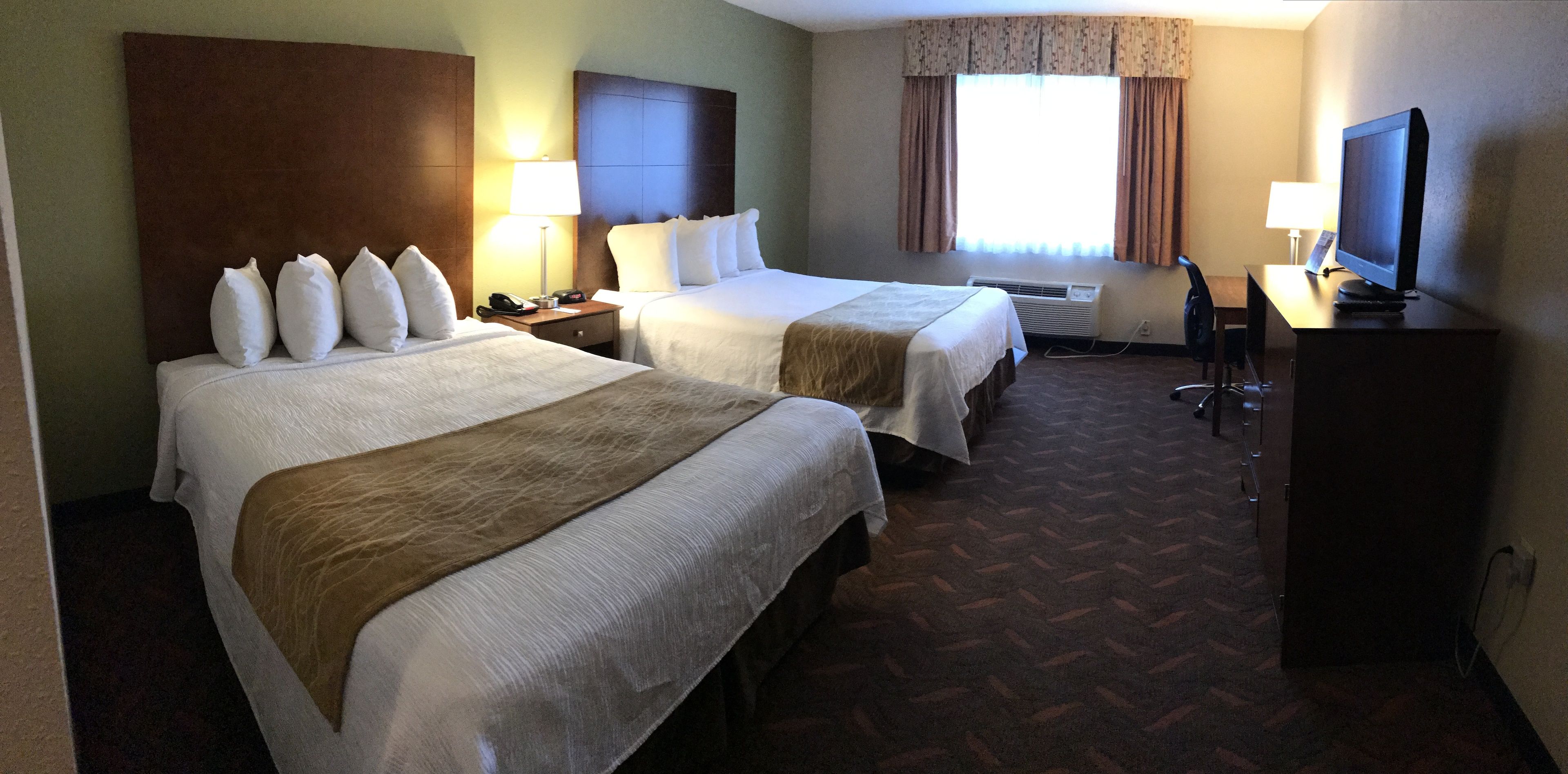 Quarto de hotel com duas camas, uma escrivaninha com computador, televisão e janela com cortinas.