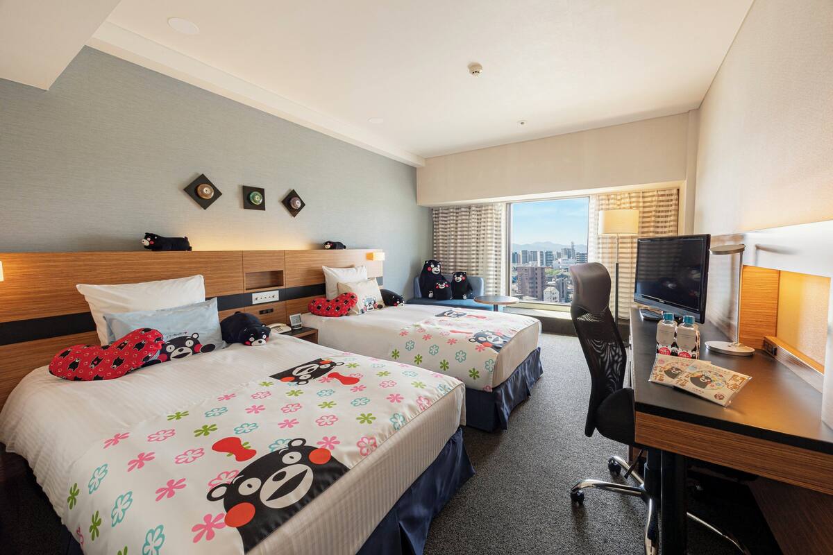 Ein Hotelzimmer mit zwei Betten, einem Schreibtisch, einem Stuhl, einem Fernseher und einem großen Fenster mit Blick auf die Stadt.