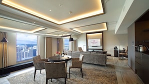 Habitación de hotel moderna con zona de comedor, un conjunto de sofás y un amplio ventanal con vistas a la ciudad.
