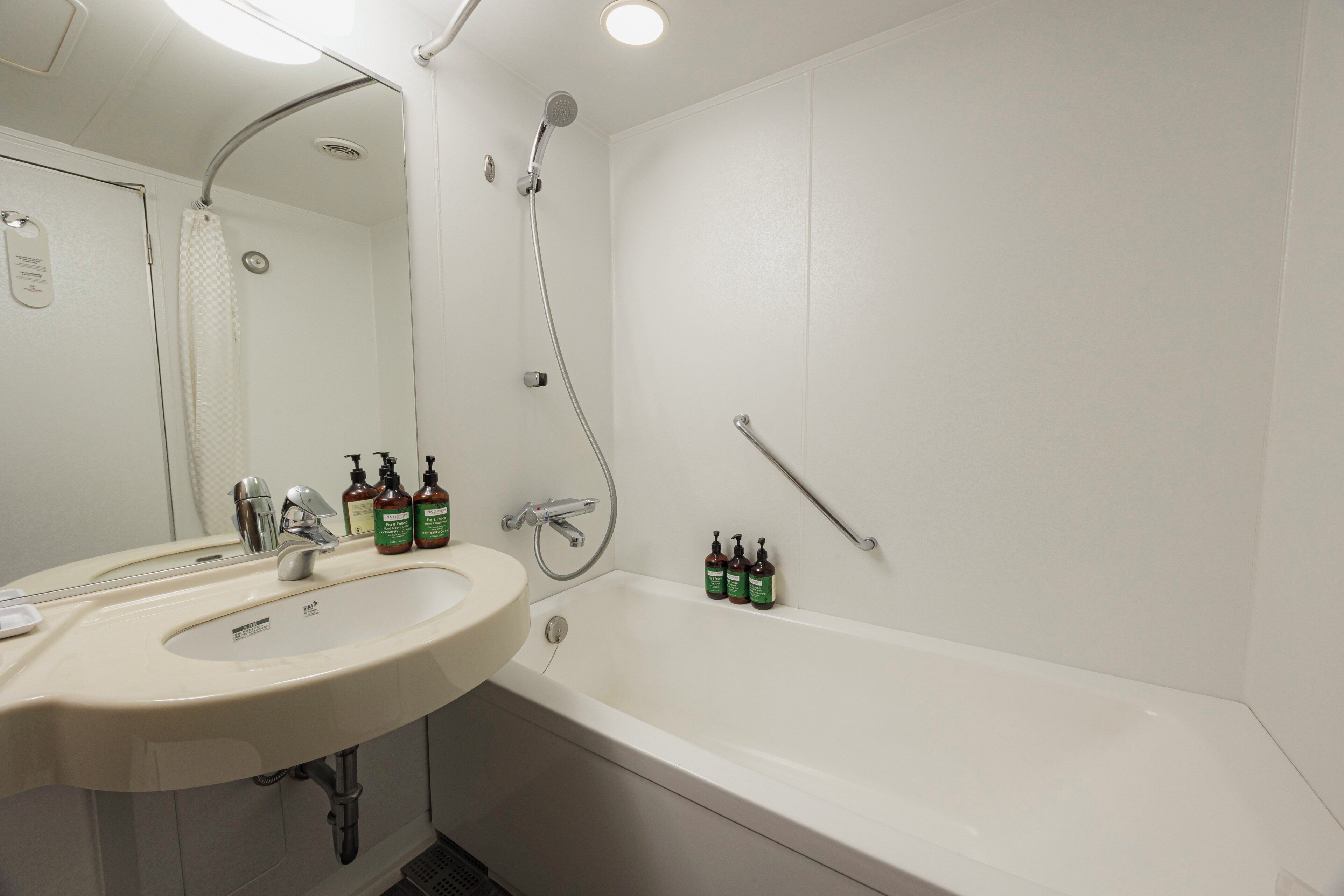 Un baño con lavamanos, espejo, ducha y dos botellas de champú.