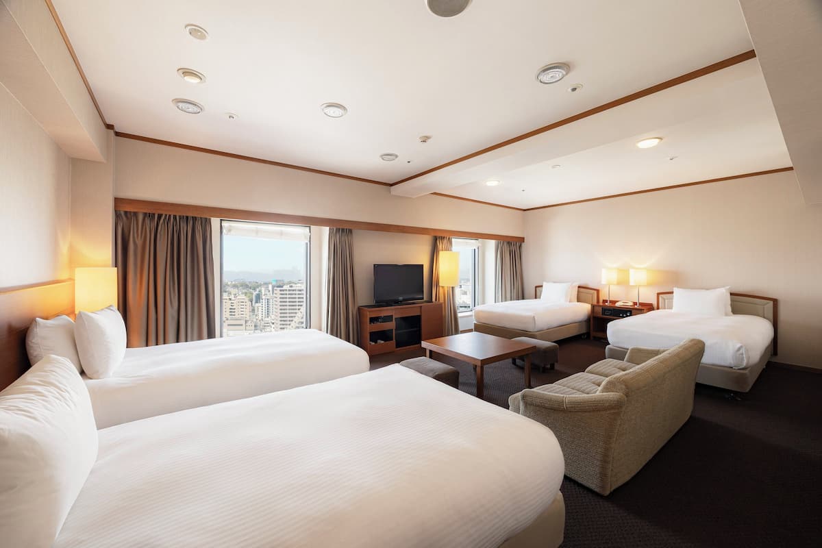 Ein Hotelzimmer mit zwei Betten, einem Fernseher, einem Schreibtisch und Blick auf die Stadt.