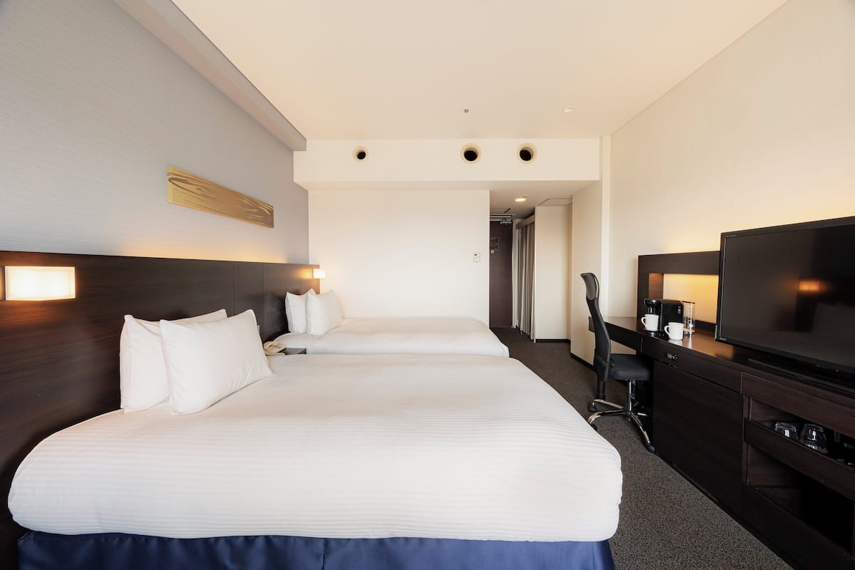 Ein Hotelzimmer mit zwei Betten, einem Schreibtisch mit Fernseher und einer Kaffeemaschine.