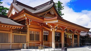 Ein traditionelles japanisches Gebäude mit einem gewölbten Dach, Holzsäulen und einer Steintreppe, die zum Eingang führt.