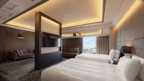 Ein modernes Hotelzimmer mit zwei Betten, einer Couch, einem Fernseher und Blick auf die Stadt.