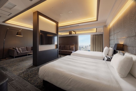 A modern hotel room with two beds, a sofa, a TV, and a city view.
