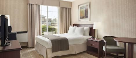 Habitación de hotel con una cama grande, un escritorio con televisión, una silla, una lámpara y una ventana con cortinas.