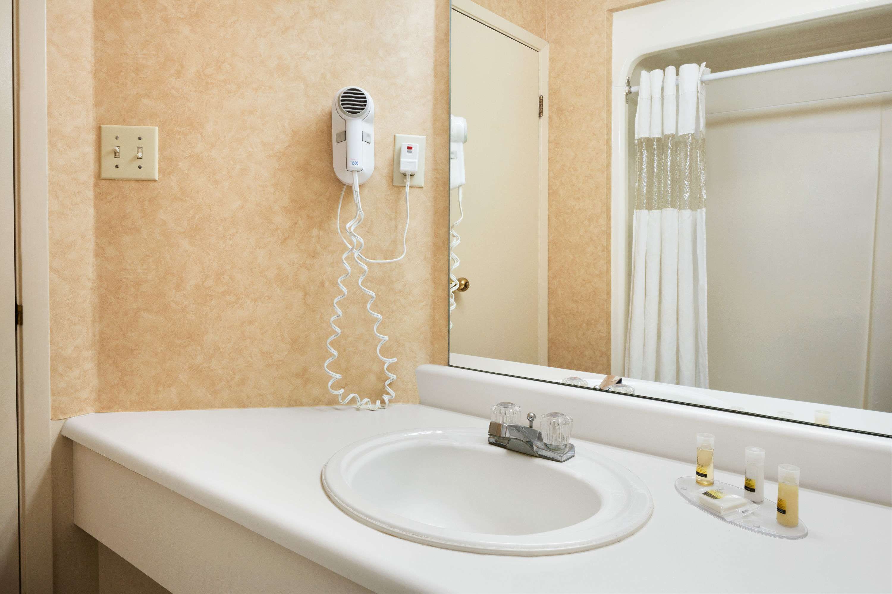 Casa de banho com lavatório branco, secador de cabelo e espelho.