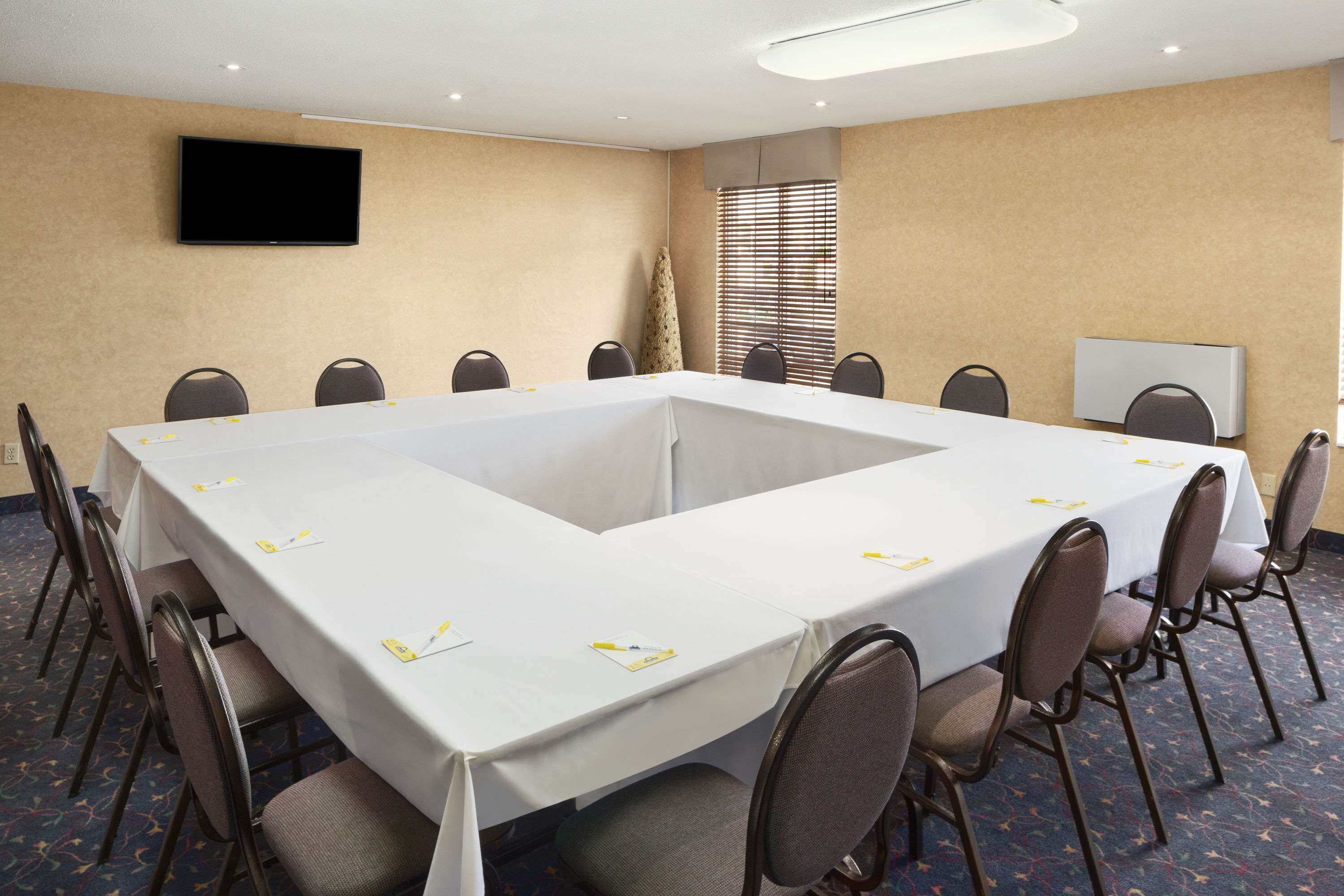Un salón de conferencias con una gran mesa, sillas, una televisión y un ventanal con persianas.