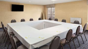 Un salón de conferencias con una gran mesa, sillas, una televisión y un ventanal con persianas.