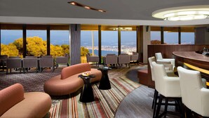 Un hall d’hôtel comprenant un bar, des espaces aménagés avec des sièges et de grandes fenêtres donnant sur la ville.