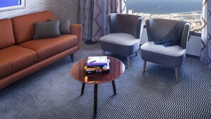 Une chambre d’hôtel moderne dotée d’une grande fenêtre donnant sur la ville, d’un canapé, de deux fauteuils, d’une petite table basse avec des livres et d’un tapis à motifs.