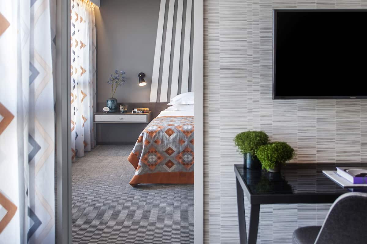 A hotel room with a bed, a desk, a TV, and a potted plant.
