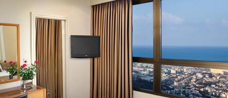 Habitación de hotel con cama, televisión, escritorio con espejo y ventana con vista a la ciudad.