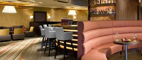 A modern lounge area with a curved sofa, bar with bottles, and a television.