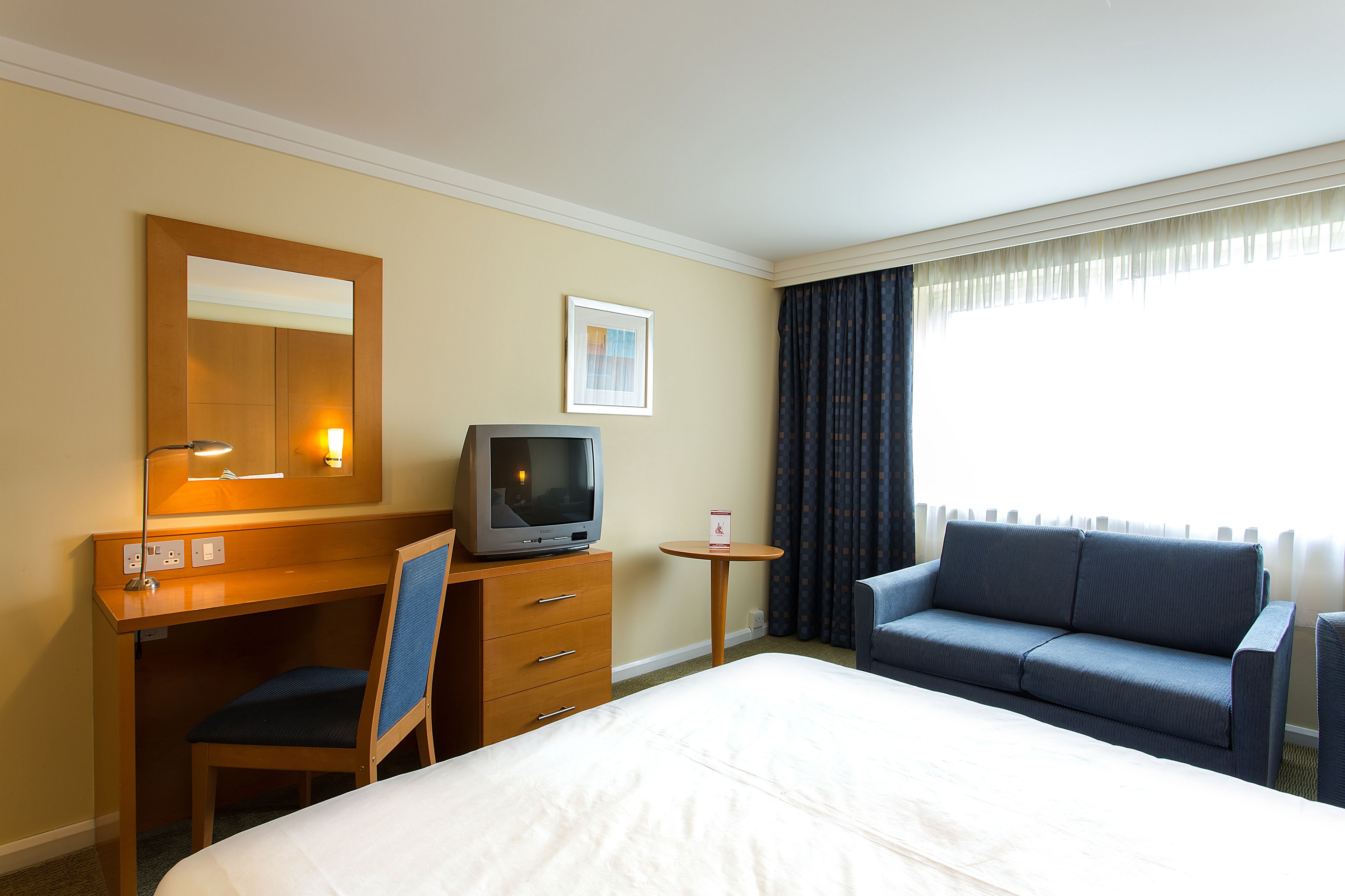 A hotel room with a bed, a desk with a chair, a television, a small table, and a sofa.