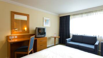 Habitación de hotel con cama, escritorio con silla, televisión, una mesita y un sofá.