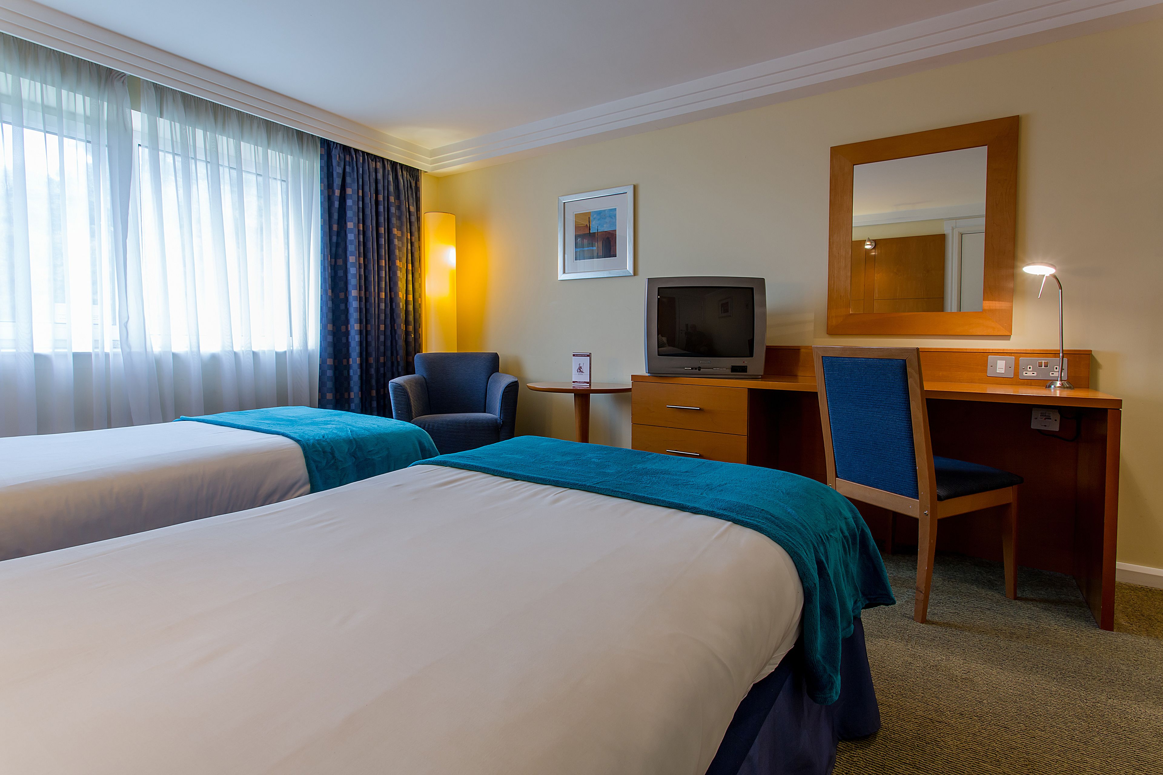 A hotel room with two beds, a desk, a chair, a television, and a large mirror.