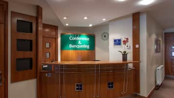 A reception area with a wooden reception desk, a green sign reading "Conference & Banqueting," and a clock on the wall.