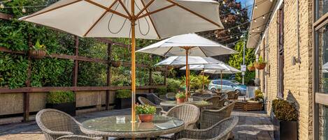 An outdoor patio with wicker furniture, white umbrellas, and hanging plants.