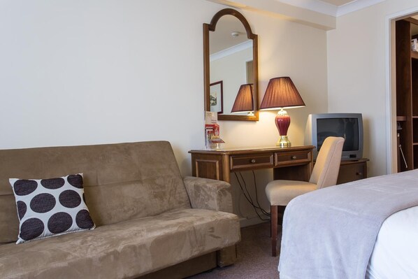 A hotel room with a sofa, a desk with a lamp, a television, and a bed.