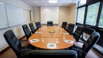 A conference room with a large table, black leather chairs, a whiteboard, and a projector screen.