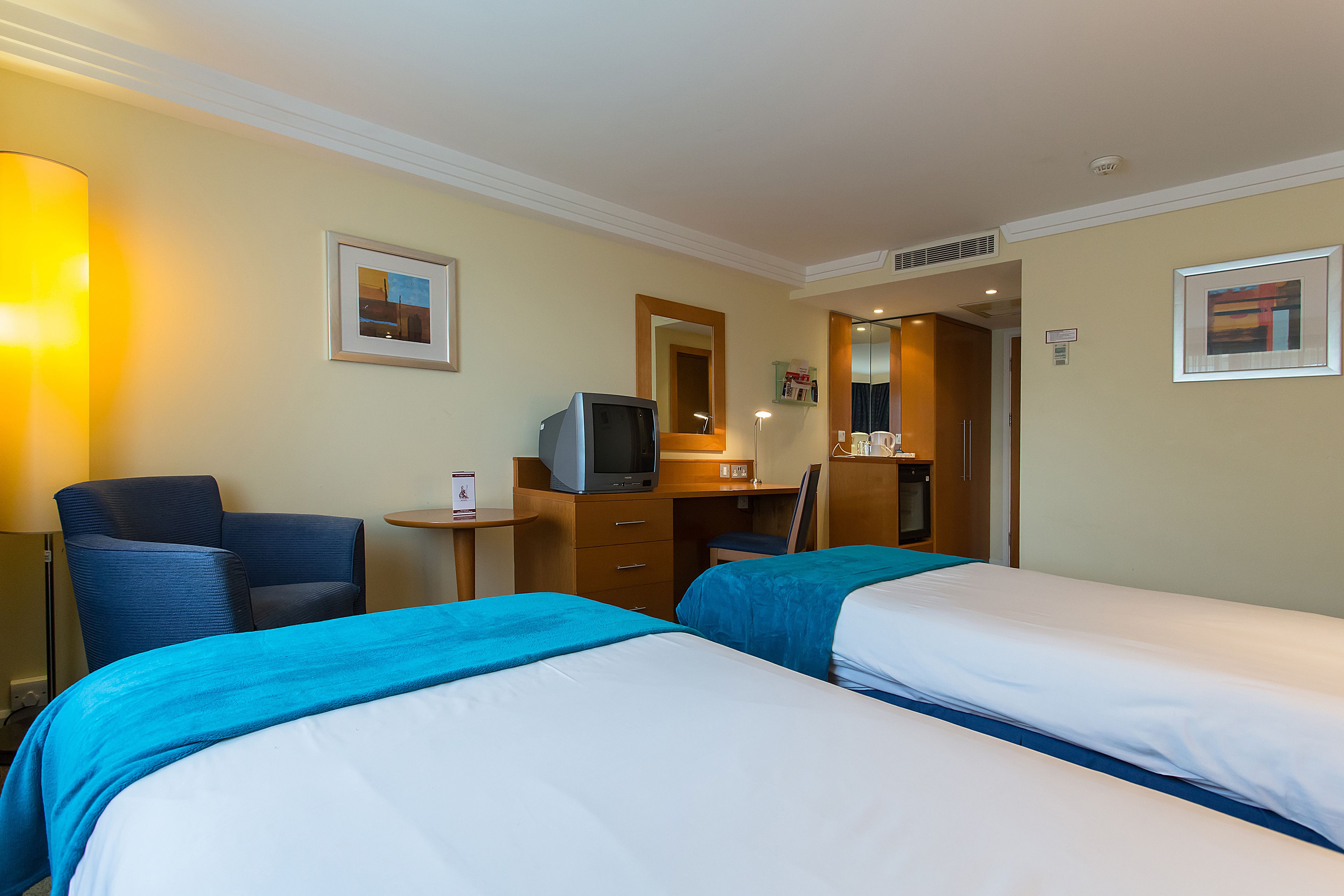 Een hotelkamer met twee bedden, een bureau met een computer, een stoel en een lamp.