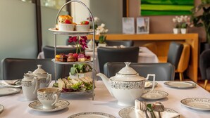 A dining table set with a tea service, a tiered dessert stand, and a floral arrangement.