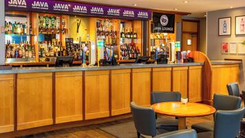 A bar area with multiple 'JAVA COFFEE LOUNGE' signs, a variety of liquor bottles, a clock, and seating with a small table and chairs.