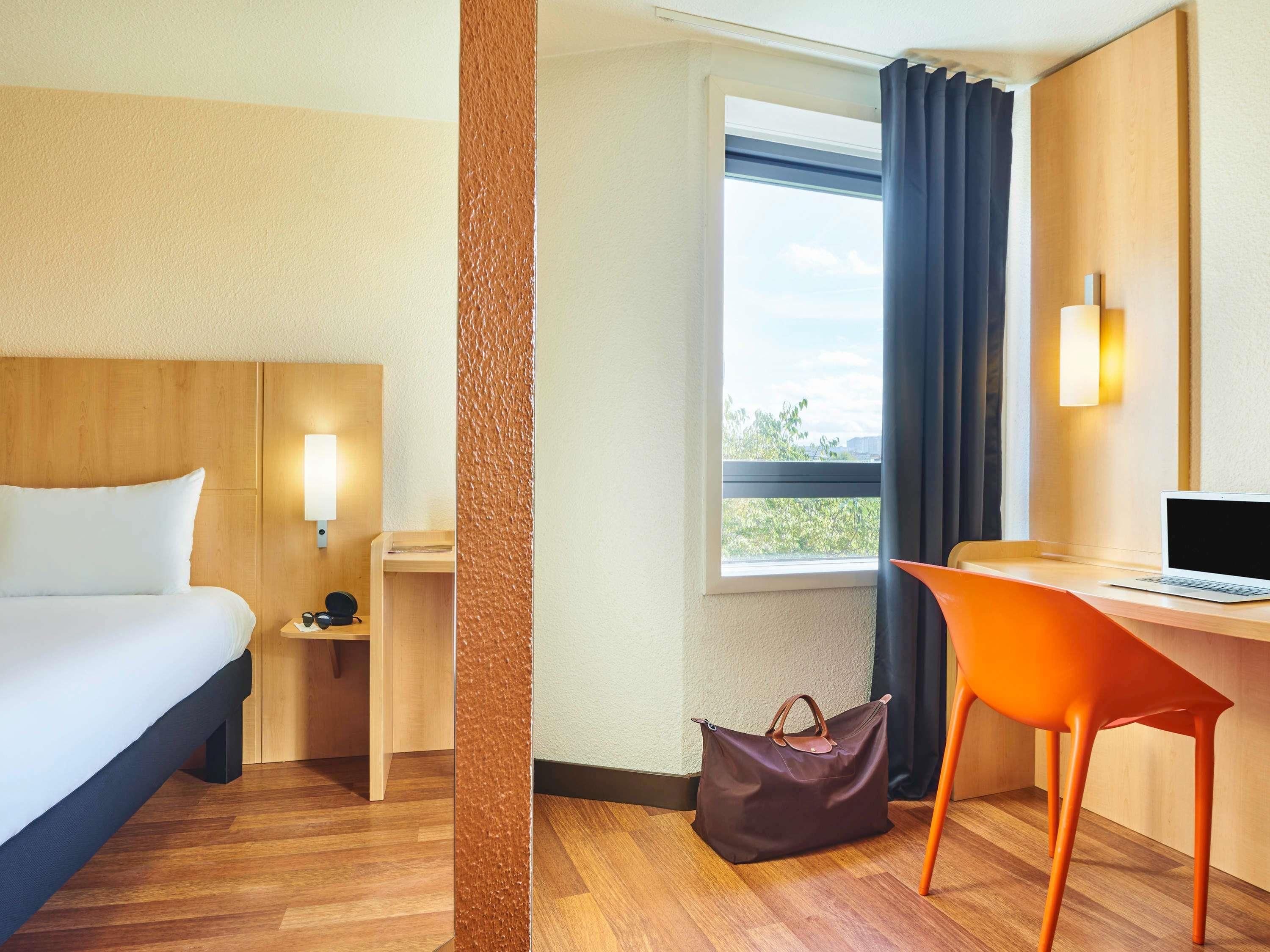 Una habitación de hotel con cama, escritorio, silla y ventana con cortinas.