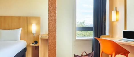 Una habitación de hotel con cama, escritorio, silla y ventana con cortinas.