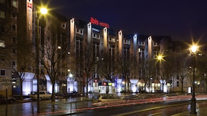 A hotel with a prominent 'ibis HOTEL' sign, multiple floors, and a parking lot with cars. - ibis Paris La Villette Cité des Sciences 19ème (Paris)