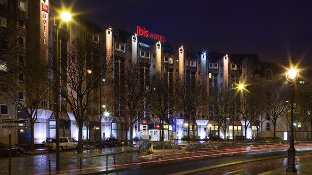 A hotel with a prominent 'ibis HOTEL' sign, multiple floors, and a parking lot with cars. - ibis Paris La Villette Cité des Sciences 19ème (Paris)